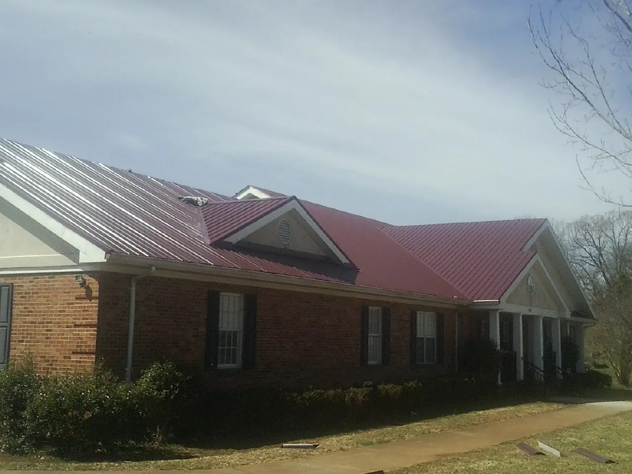 Red metal roof with gabled entries on a long brick building, from a Hail Damage Roof Repair job in Montville
