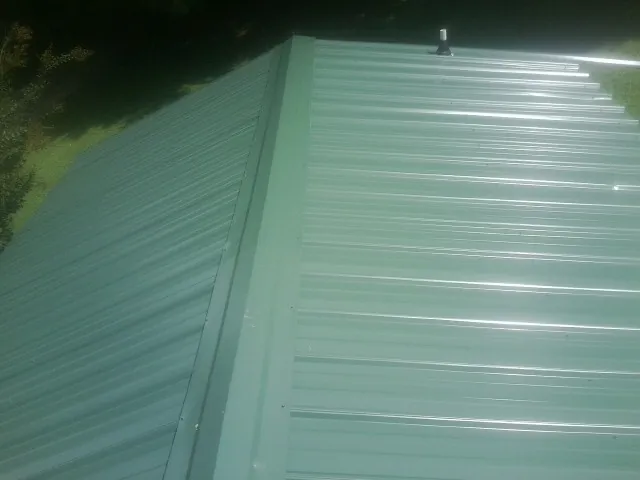 New green metal panels meeting at the ridge of a roof — Flat Roof Repair work by our crew in Montville